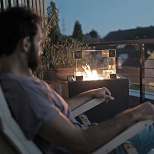 Mann auf Liegestuhl auf Terrasse. Gaskamin mit Glas im Hintergrund